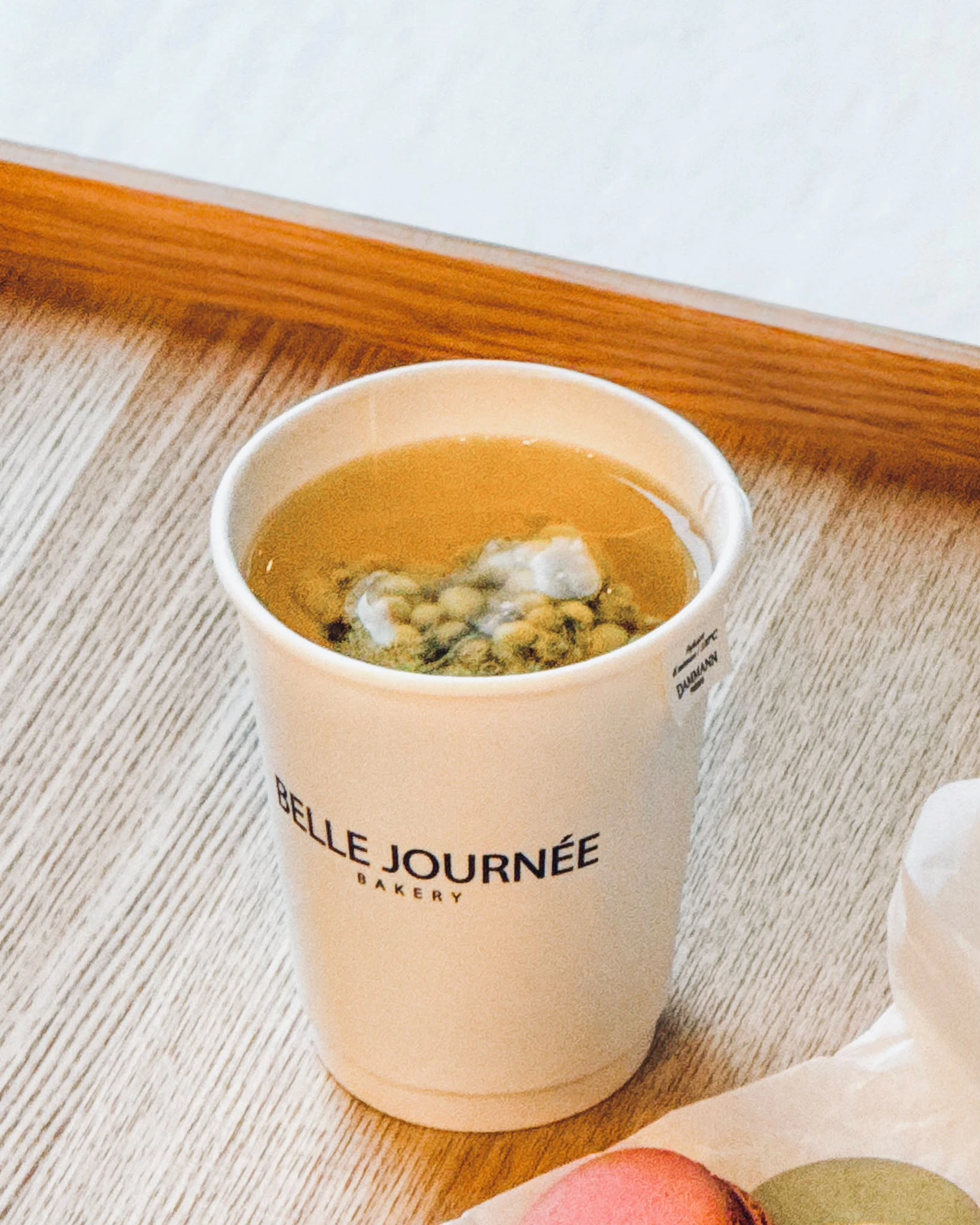 A drink in a Belle Journée Bakery branded cup on a wooden table.