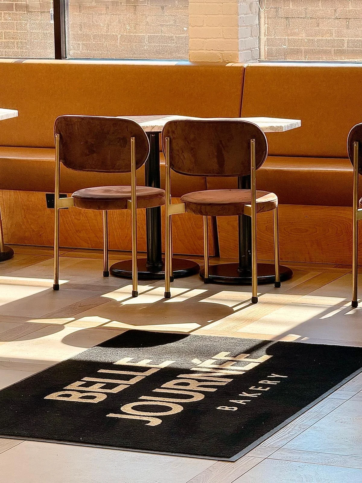 Sunlight on the café floor and Belle Journée floor mat beneath the seating.